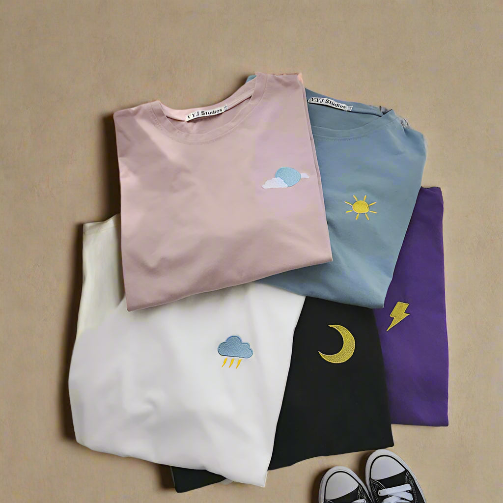 Stack of folded t-shirts with embroidered designs on a white surface.
