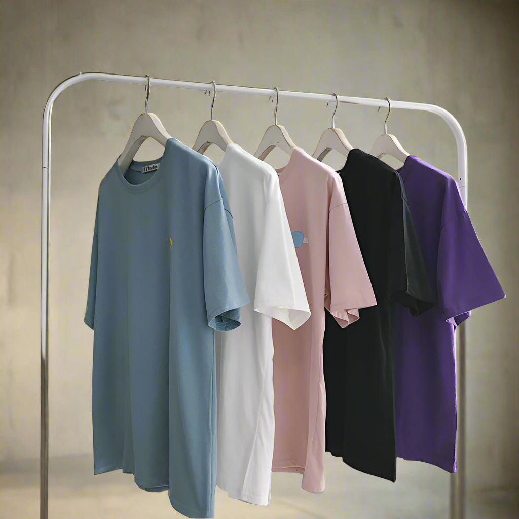 Five shirts in blue, white, pink, black, and purple hanging on a rack against a white wall.